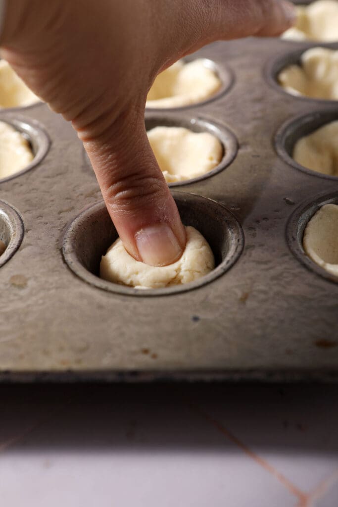 a thumb presses a ball of dough into the basin of a mini muffin tin to make an individual pie crust