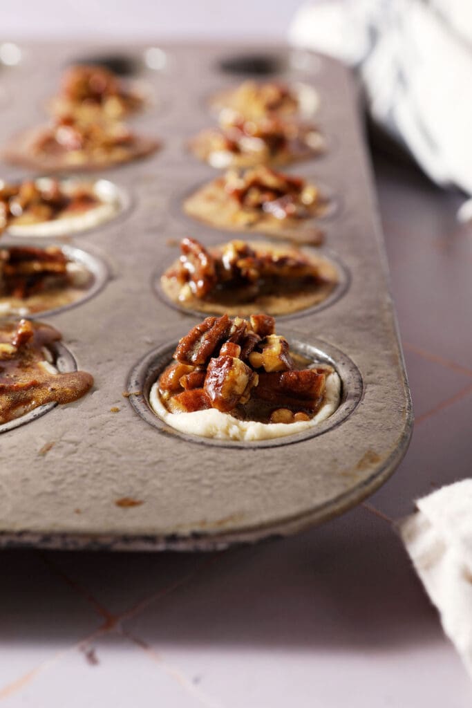 pecan pie filling sits on top of mini muffin cups in a mini muffin tin before baking