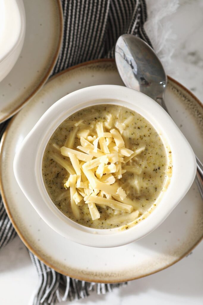 Close up of a white bowl holding a serving of Easy Broccoli Cheddar Soup garnished with additional cheese