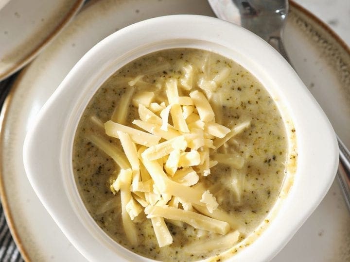 Close up of a white bowl holding a serving of Easy Broccoli Cheddar Soup garnished with additional cheese