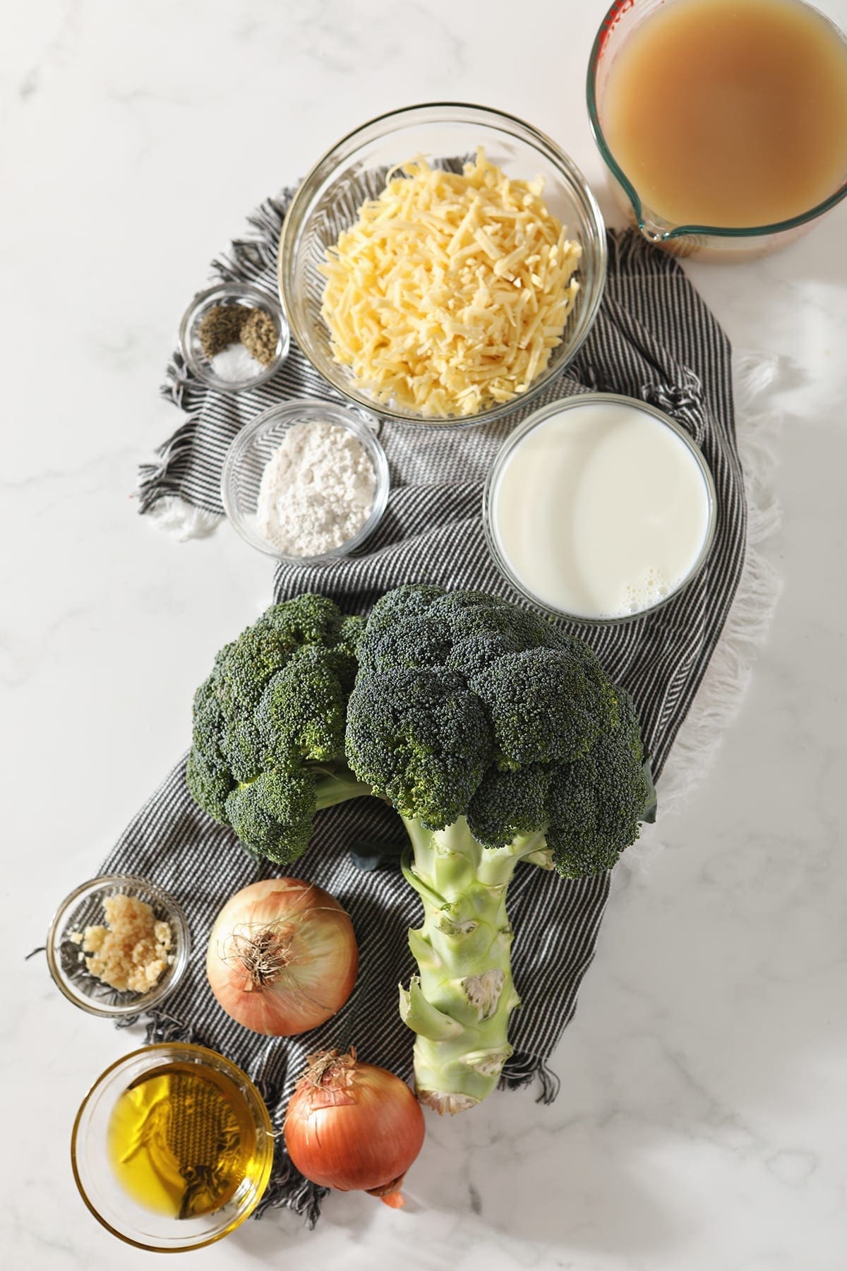 Ingredients for broccoli cheddar soup on a marble countertop in bowls