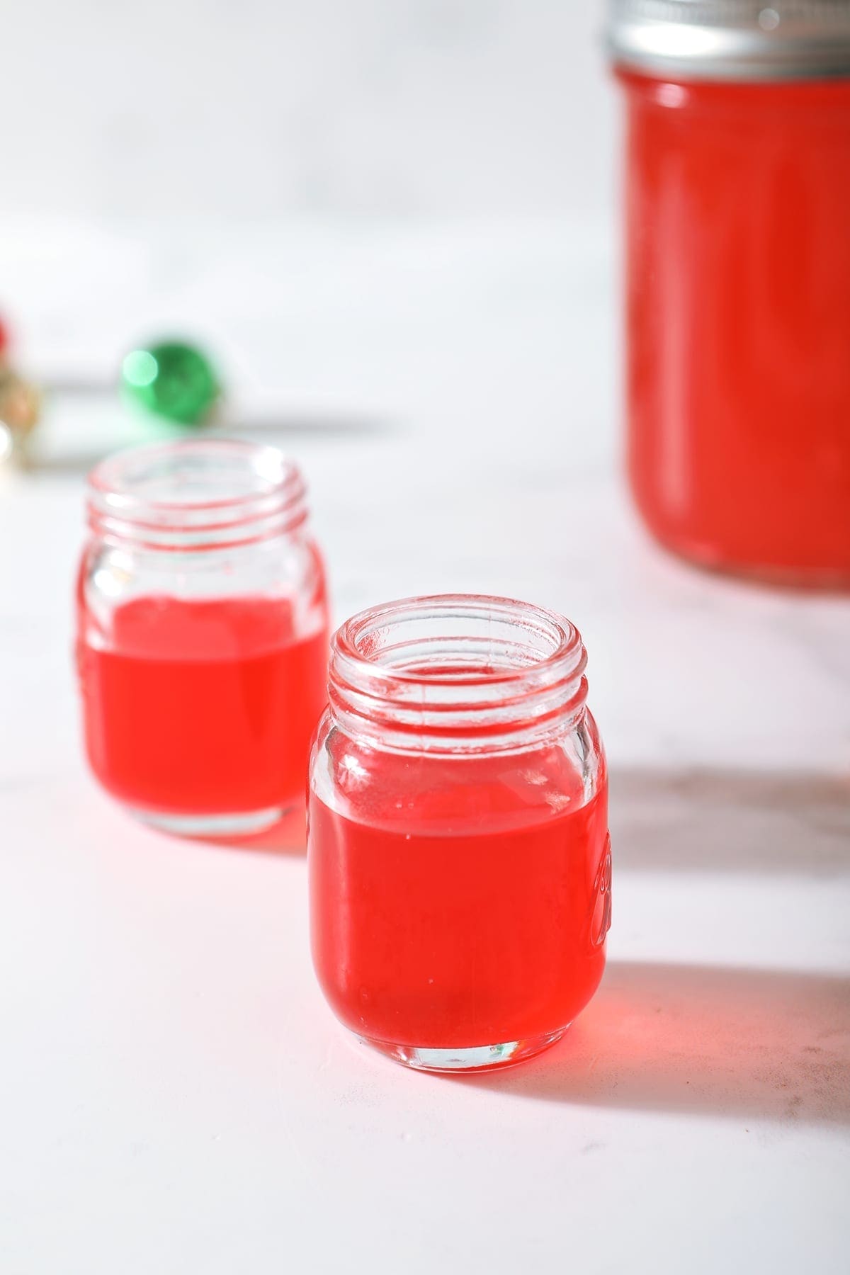 Two shot glasses of peppermint vodka on a marble surface next to a mason jar full of the candy cane-infused vodka