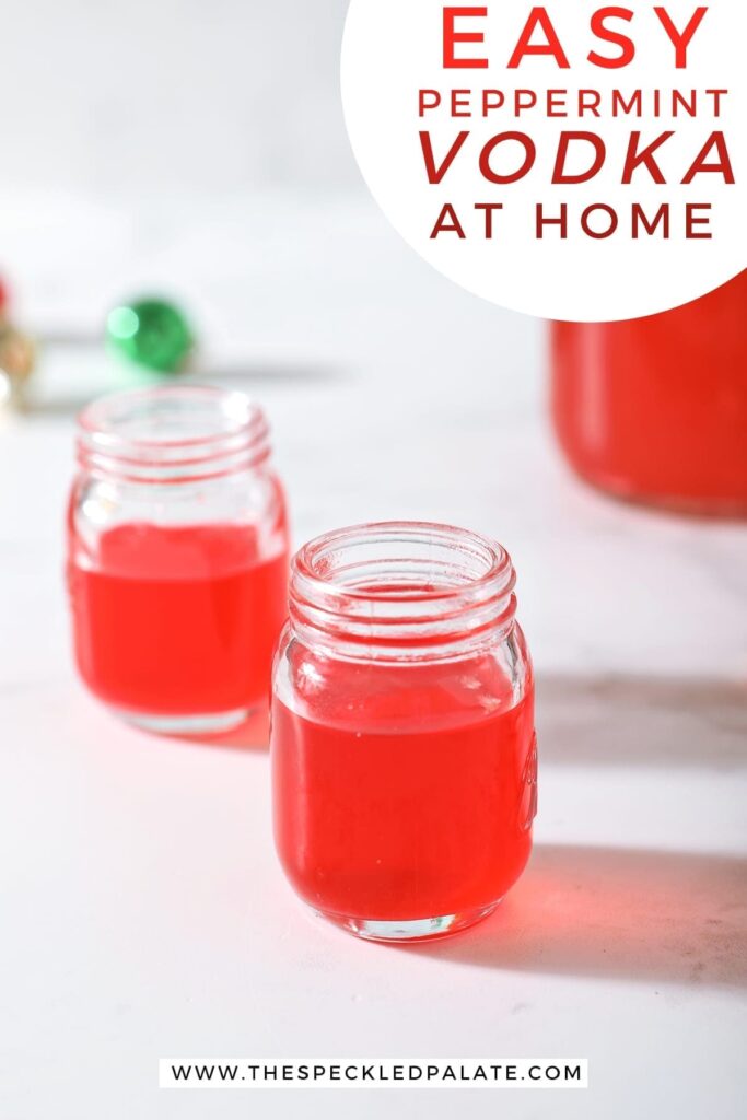 Two shot glasses of peppermint vodka on a marble surface next to a mason jar full of the candy cane-infused vodka with the text 'easy peppermint vodka at home'