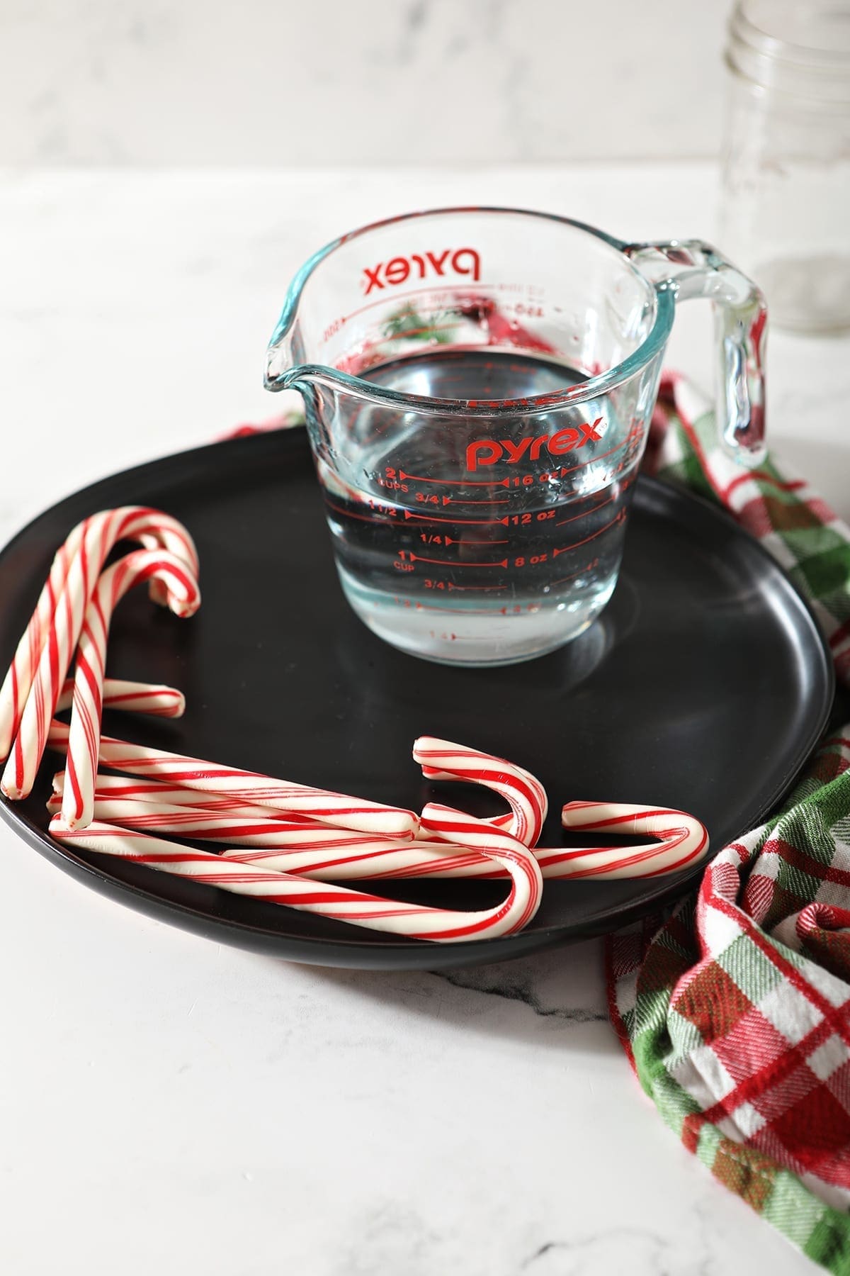 a measuring cup with peppermint vodka on a black plate with peppermint sticks