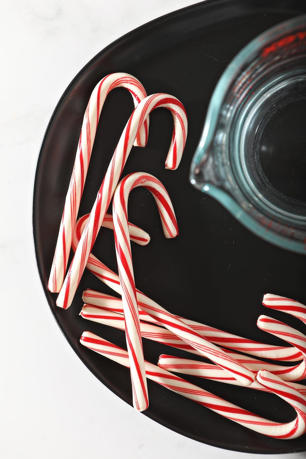 Close up of candy canes next to a measuring cup of vodka on a black plate