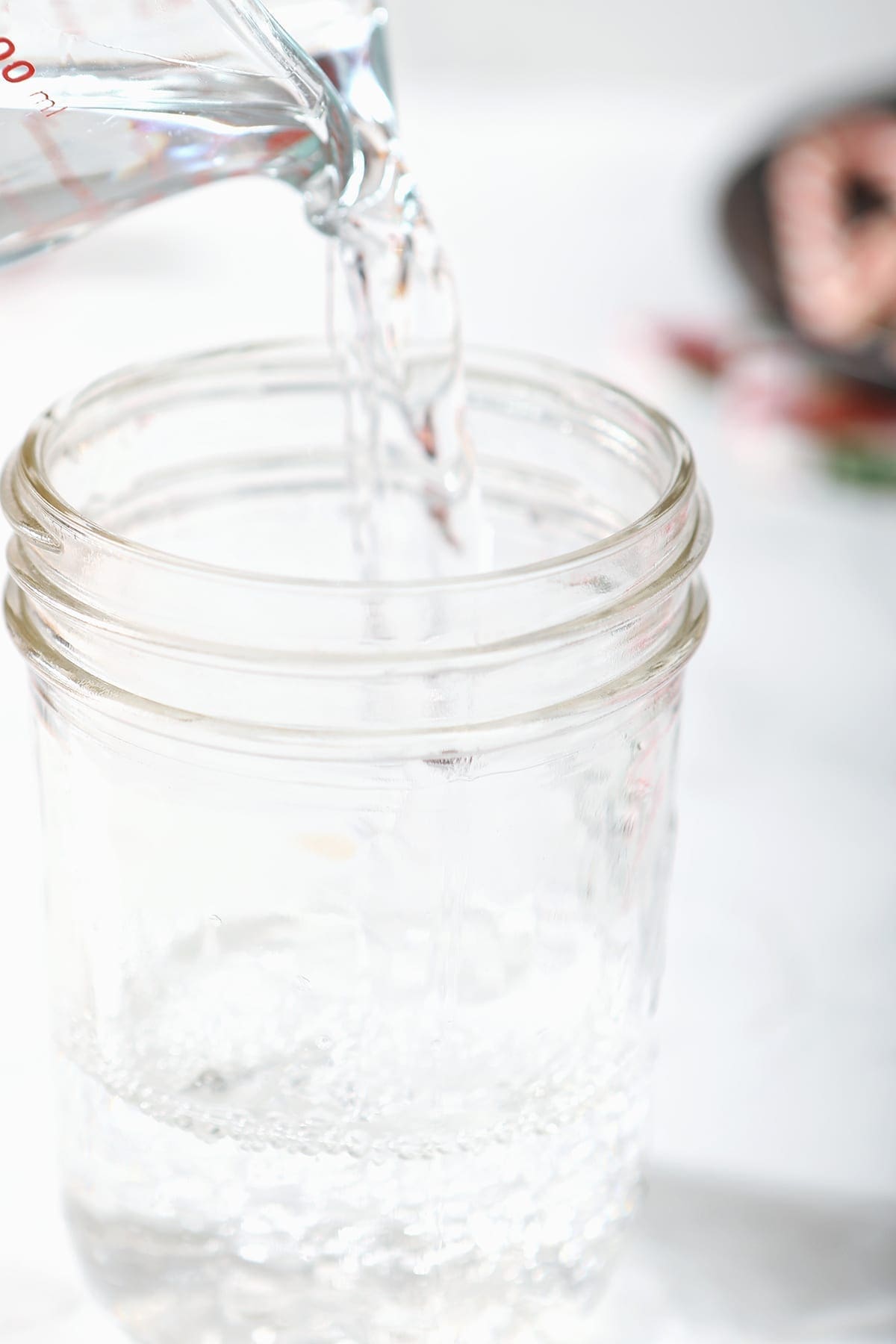 Vodka pours into a mason jar on a marble surface