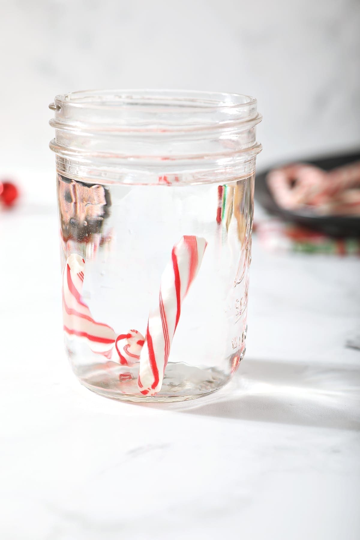 A single broken candy cane in a jar full of vodka on a marble surface