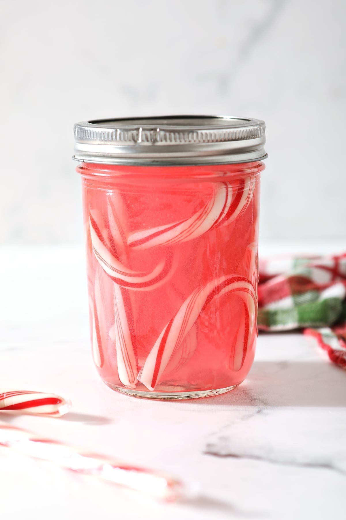 Partially dissolved candy canes in a sealed mason jar of vodka on a marble surface