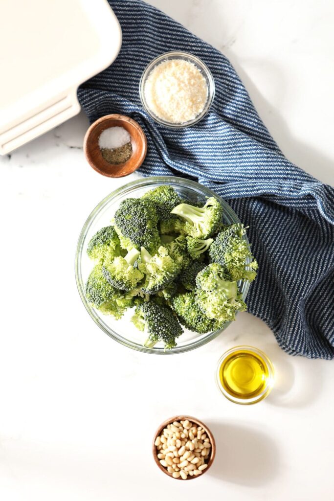 Ingredients for roasted broccoli with parmesan and pine nuts on marble with a dark blue towel