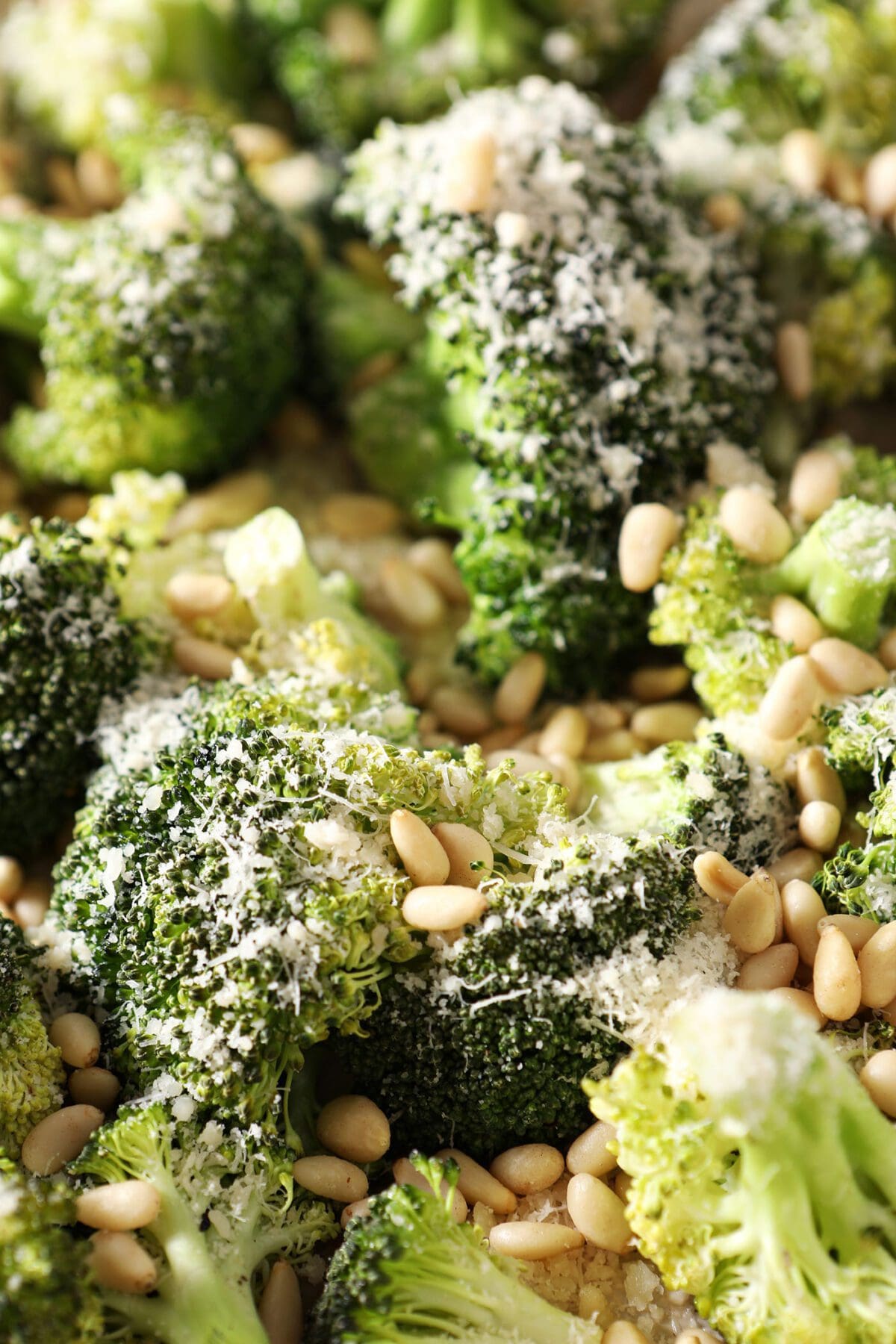 Close up of broccoli topped with parmesan and pine nuts before roasting