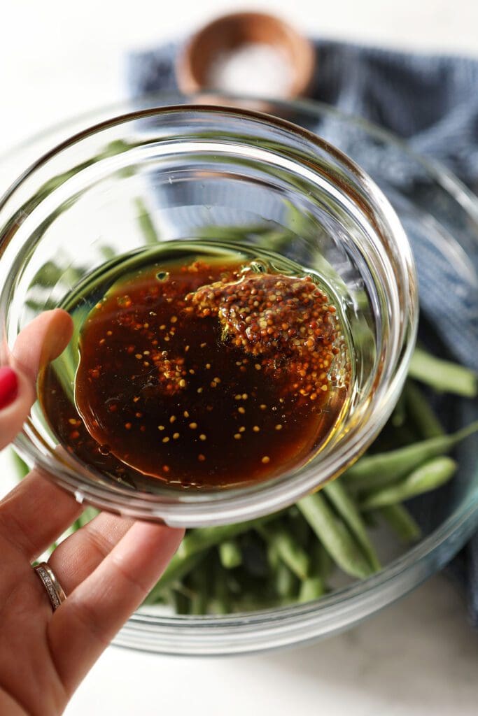 Dressing ingredients in a glass bowl above a bowl of green beans