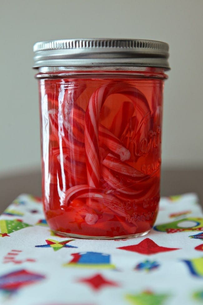 Candy canes are shown inside a mason jar as they infuse with vodka to make Candy Cane Vodka