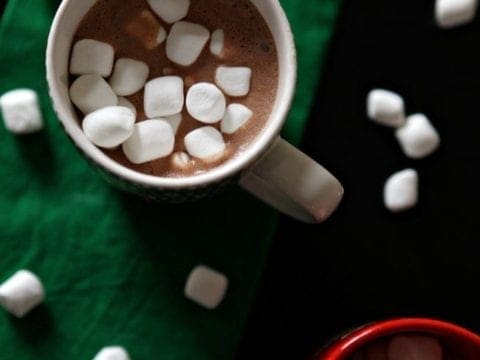 Overhead of two mugs holding dairy free hot chocolate with mini marshmallows in the mugs sitting on a green cloth