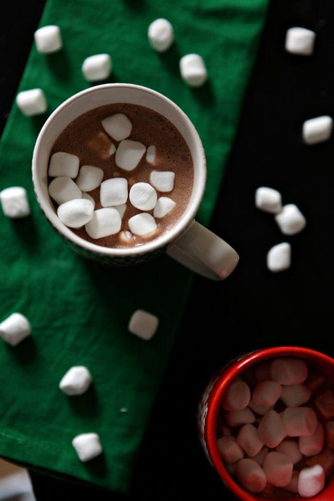 Overhead of two mugs holding dairy free hot chocolate with mini marshmallows in the mugs sitting on a green cloth