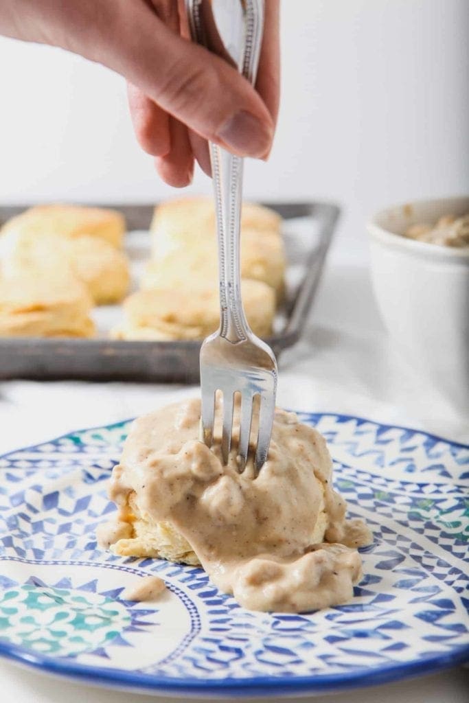 A fork cuts into Cream Biscuits, topped with decadent White Sausage Gravy, at brunch