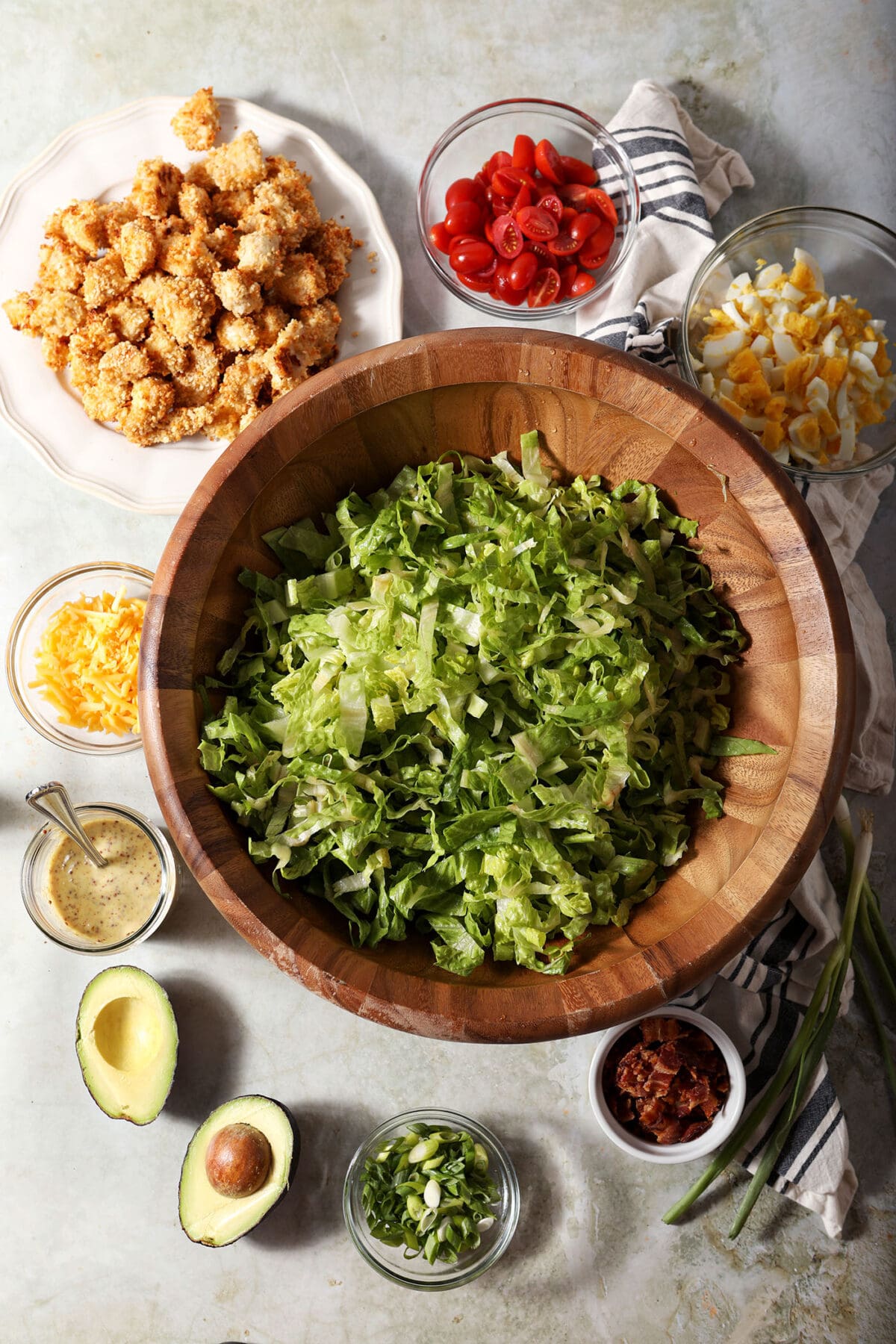 ingredients to make chicken cobb salad on a green surface with a white and black striped linen