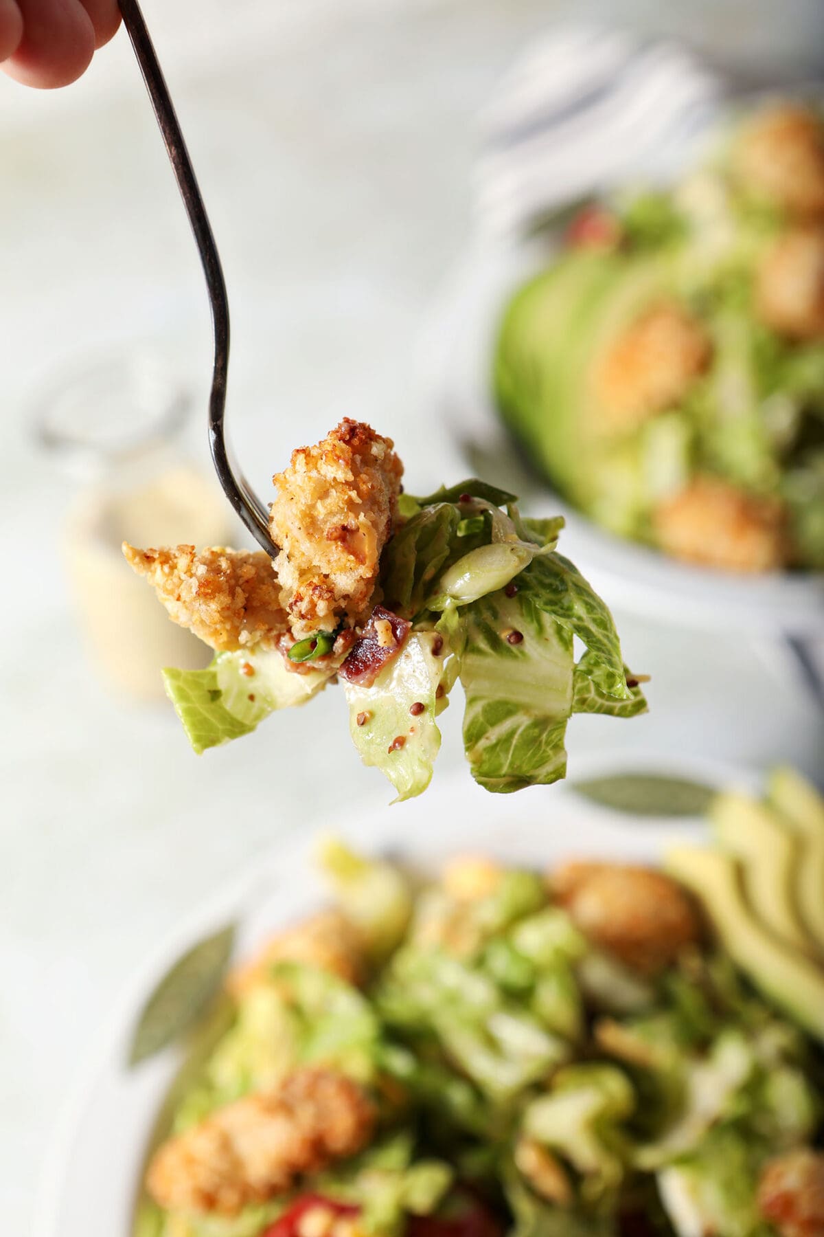 a fork holds a bite of a chicken cobb salad above bowls