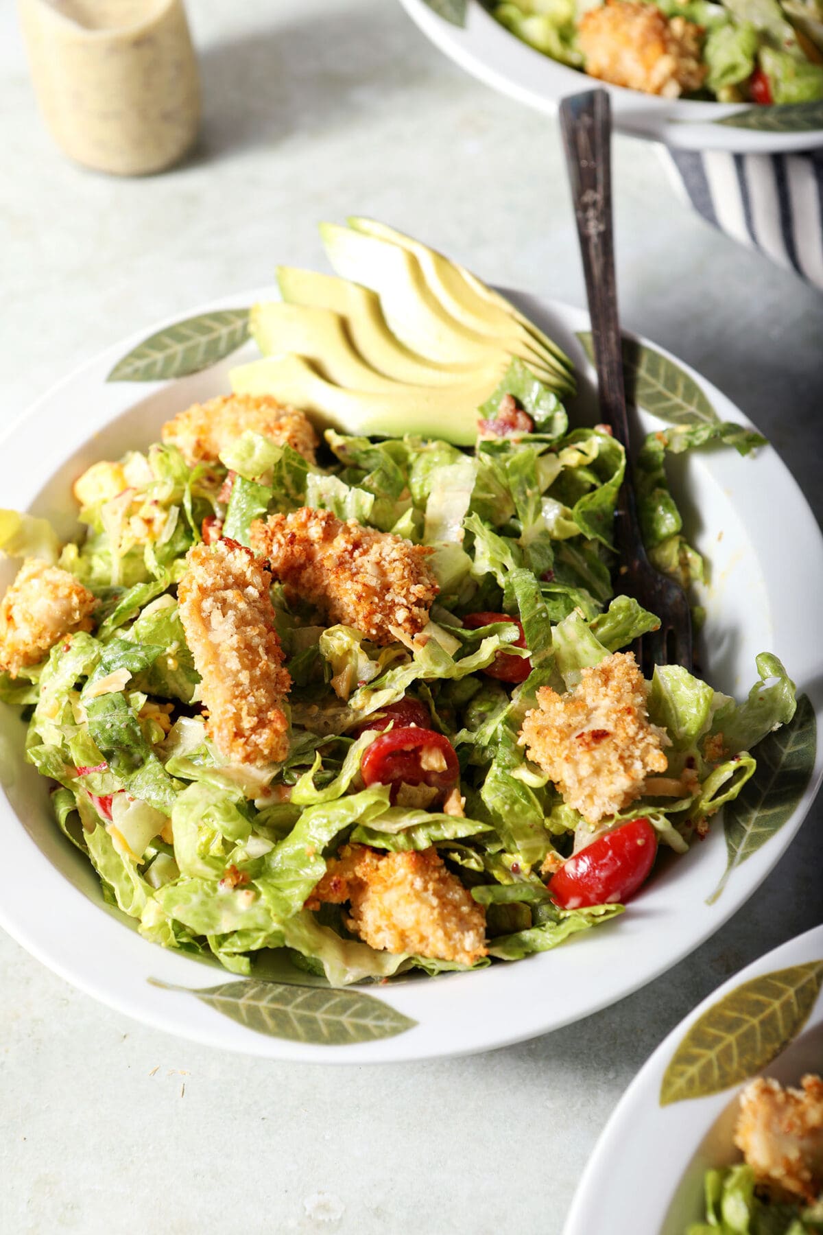 close up of a bowl of crispy chicken cobb salad with a fork in it on a green surface