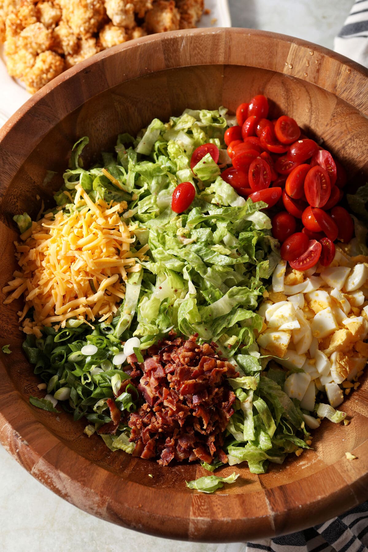 ingredients for cobb salad in a large wooden bowl before tossing