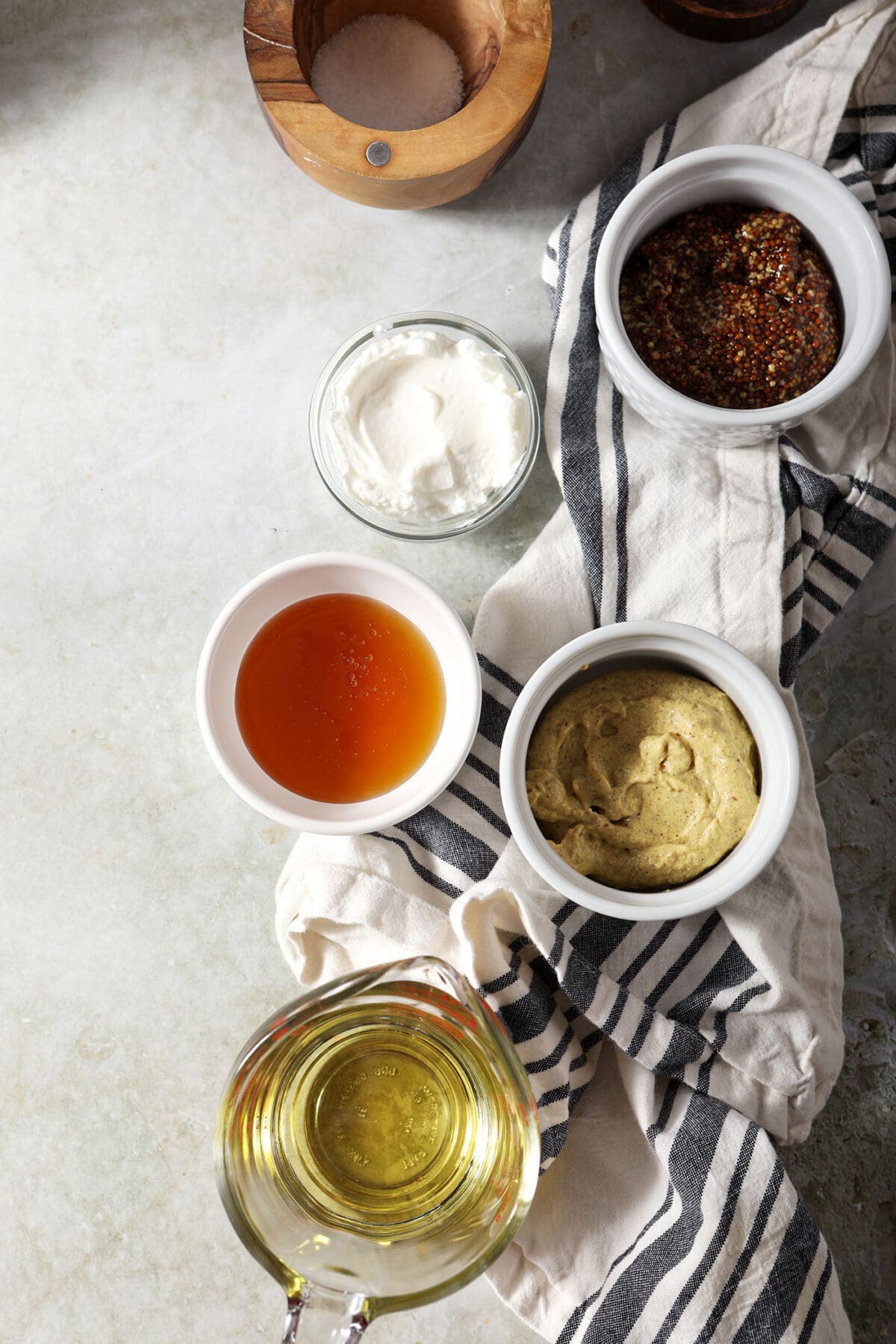 Ingredients to make honey mustard dressing in bowls on a green surface with a white and black striped linen