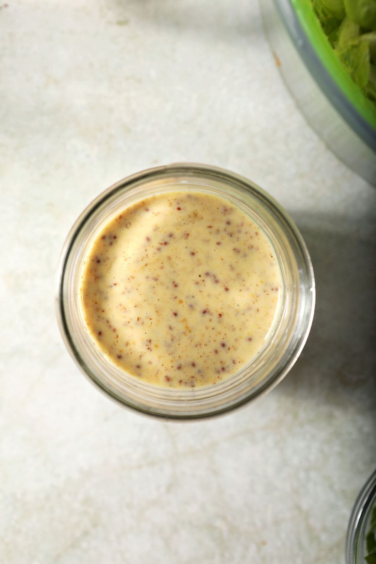 Overhead of a jar of Creamy Honey Mustard Dressing on a green surface