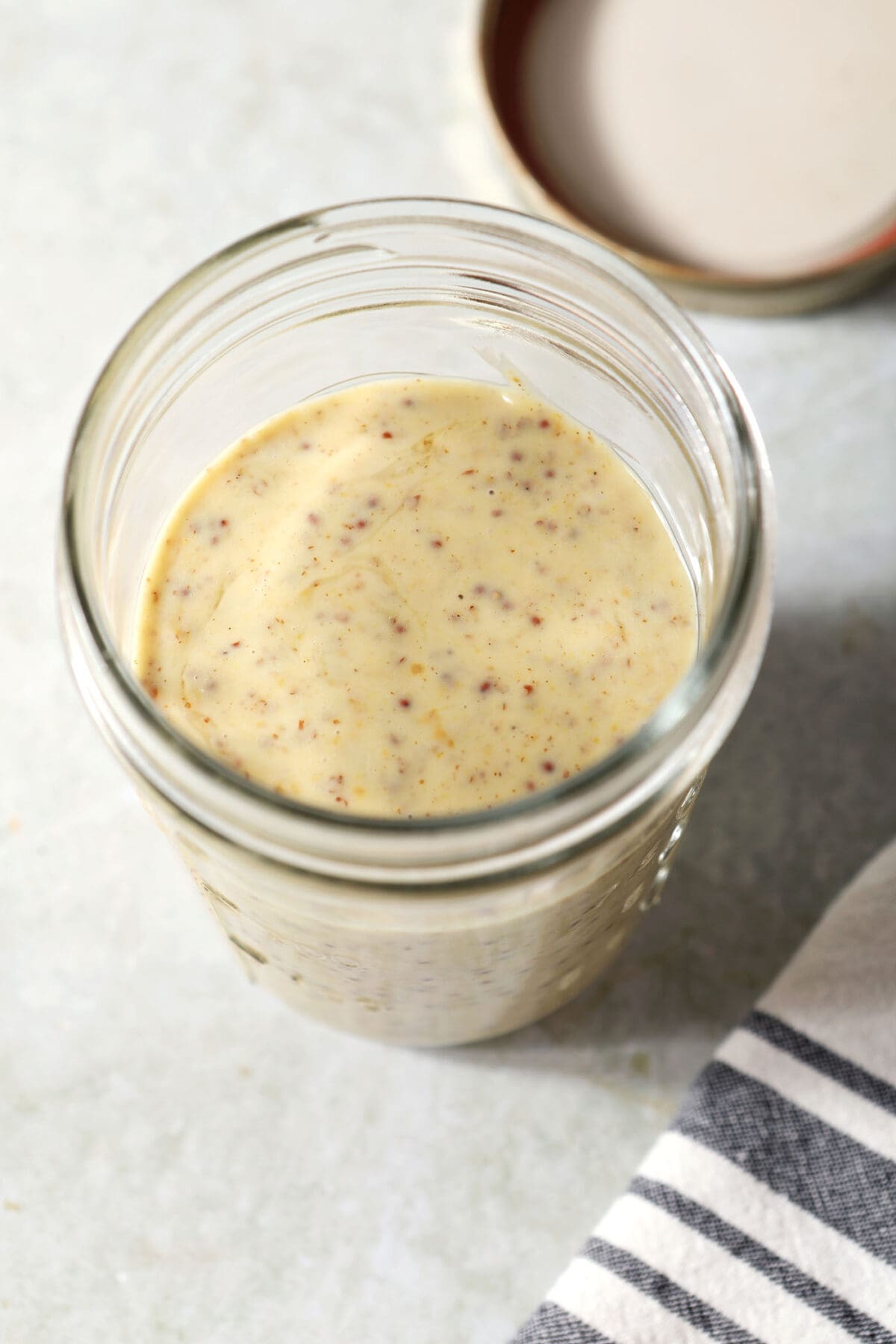 Side angle of honey mustard dressing in a mason jar next to a black and white striped linen on an olive green surface