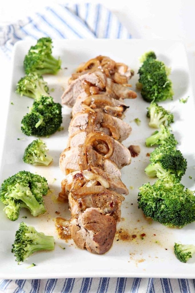 Leigh's Everything-but-the-Kitchen-Sink Pork Tenderloin laid out, in rounds, on a white platter with broccoli