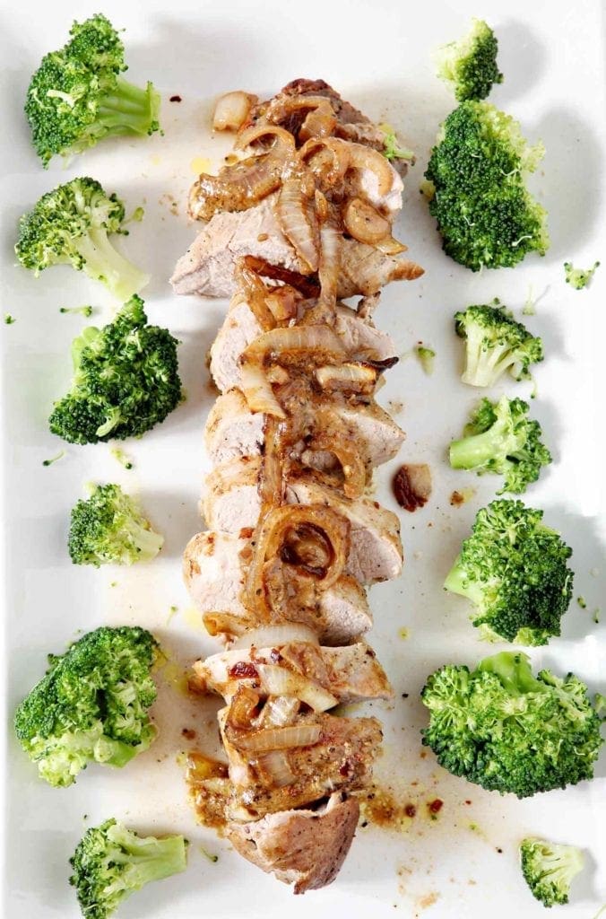 Overhead shot of Leigh's Everything-but-the-Kitchen-Sink Pork Tenderloin laid out, in rounds, on a white platter with broccoli