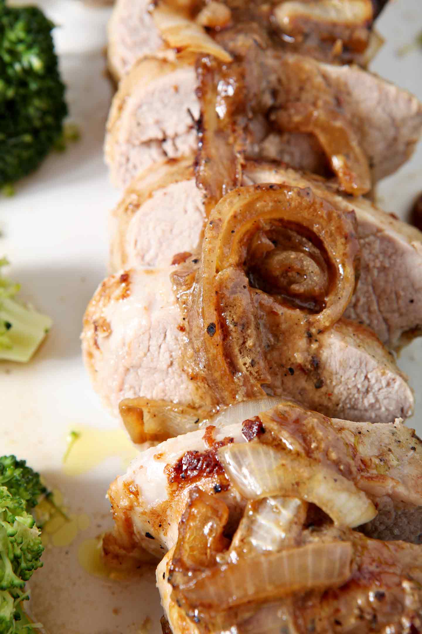 Close-up shot of Leigh's Everything-but-the-Kitchen-Sink Pork Tenderloin laid out, in rounds, on a white platter with broccoli