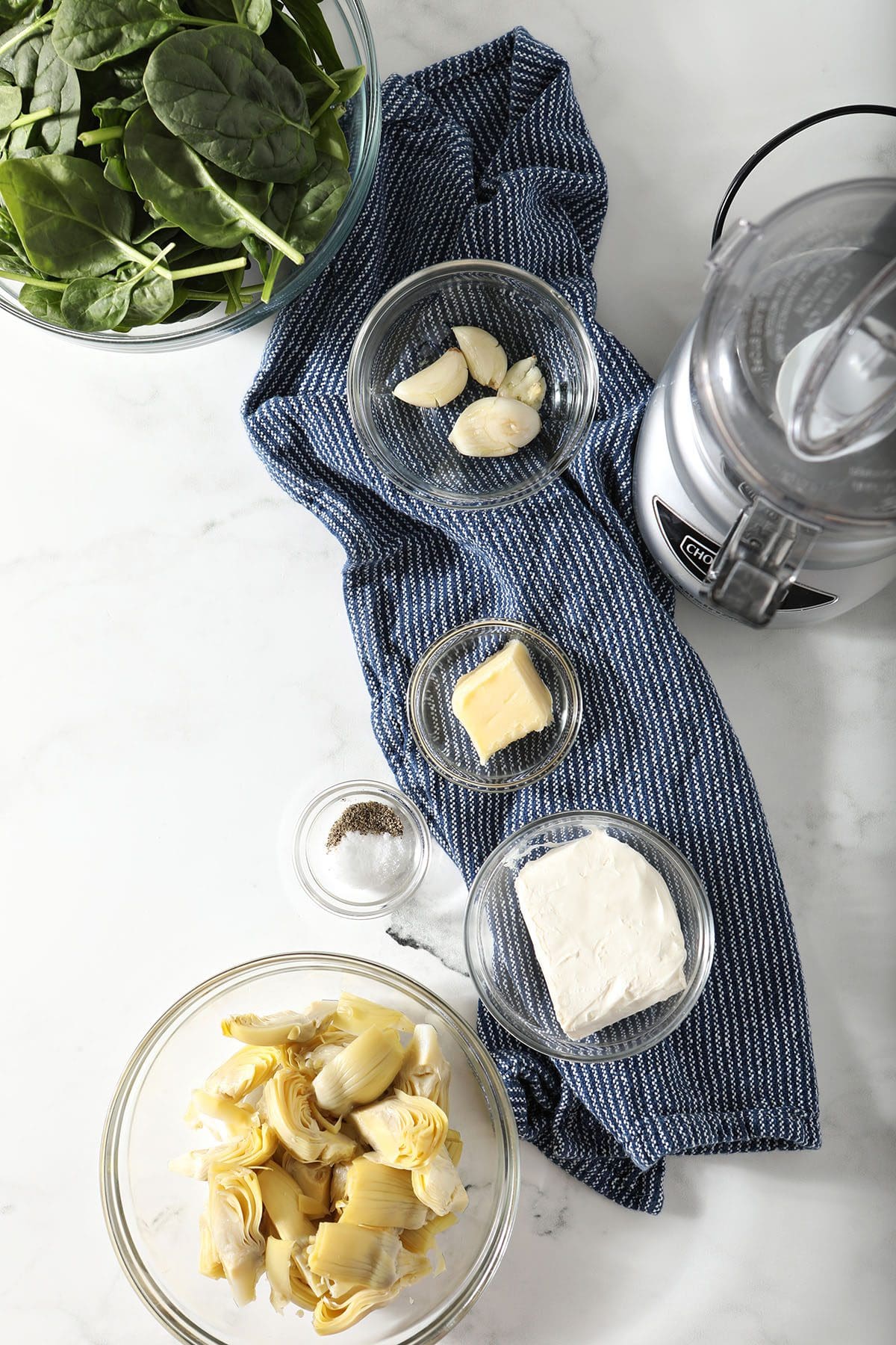 Ingredients to make a spinach artichoke burger filling in bowls on a marble countertop