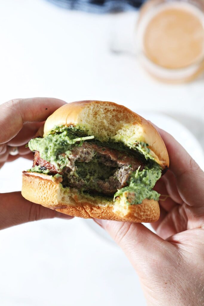 A man holds a bitten-into burger topped with spinach-artichoke dip