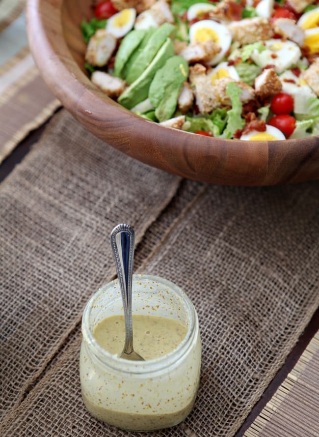 Wood bowl filled with salad behind a jar of dressing 