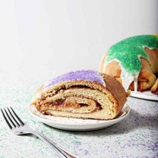 A slice of Cream Cheese and Raspberry King Cake sits in front of the whole King Cake