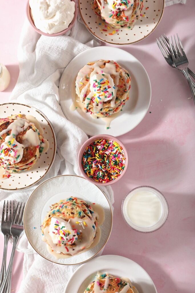 Five plates of confetti pancakes with whipped cream and vanilla glaze