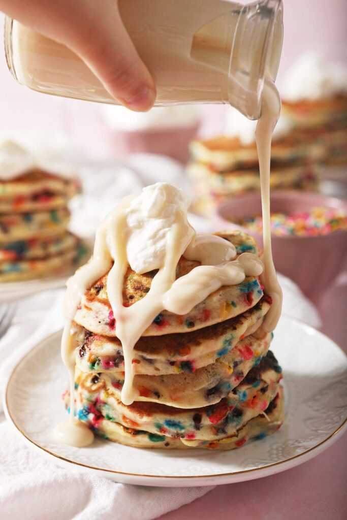 Vanilla glaze drizzles onto a stack of birthday cake pancakes