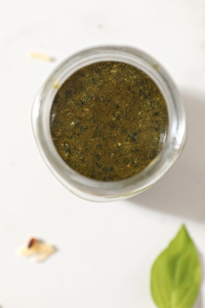 A jar of homemade basil pesto on marble