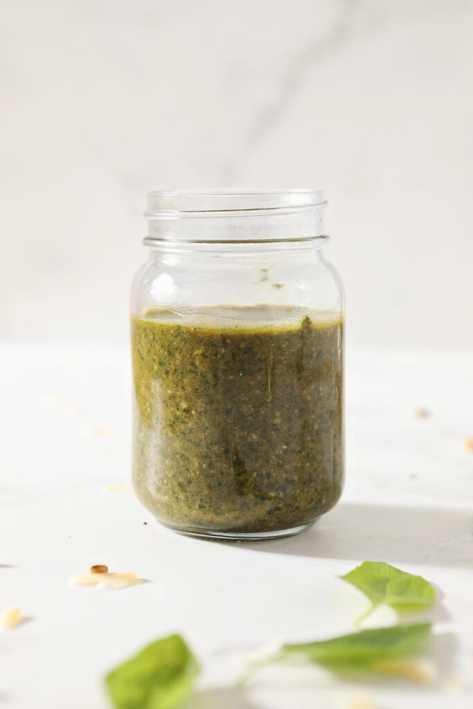 A jar of homemade basil pesto on marble