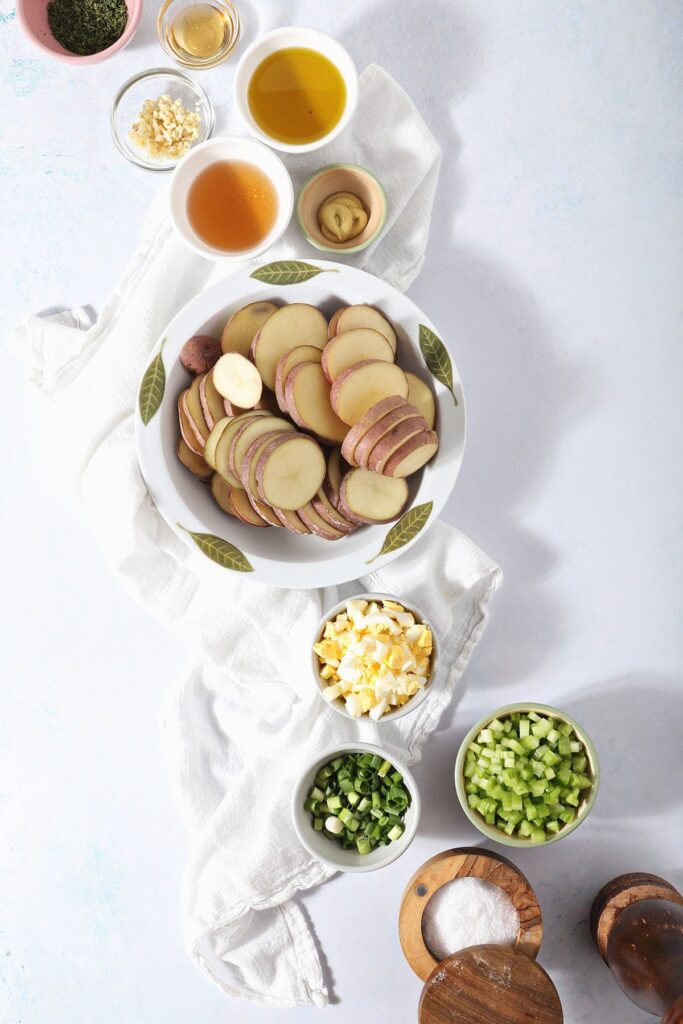 Sliced red potatoes with other homemade potato salad ingredients in bowls