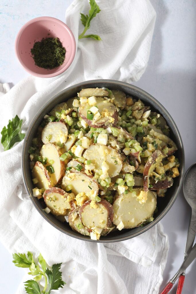 A bowl of no mayo potato salad on a white towel with tongs