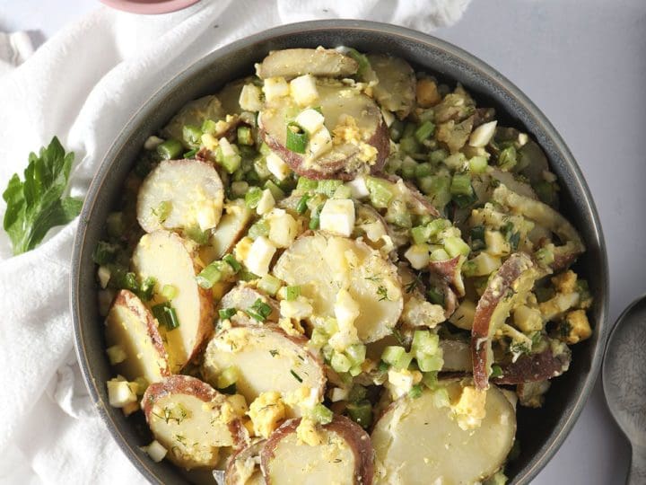 A bowl of no mayo potato salad on a white towel with tongs