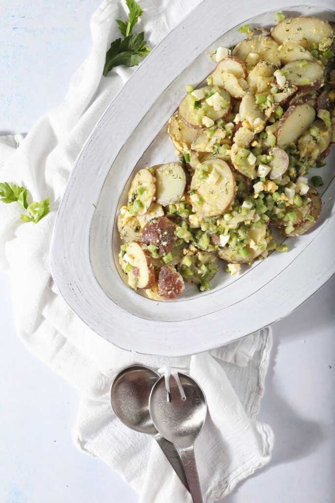 A serving platter of homemade potato salad with salad tossers