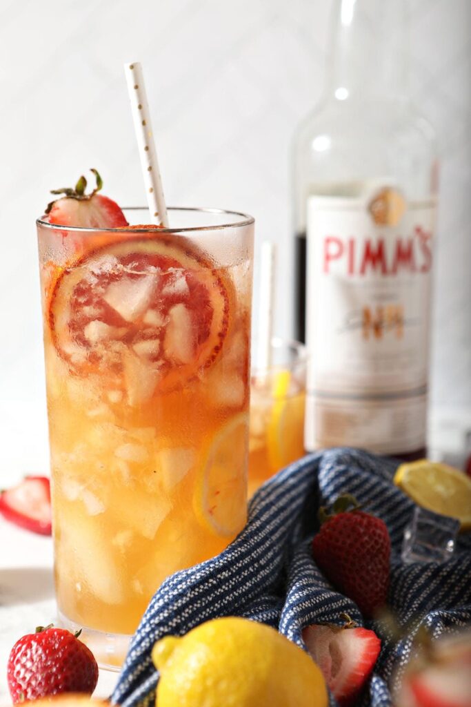 A glass of Pimms Punch garnished with strawberry and blood orange in front of a Pimm's No. 1 bottle