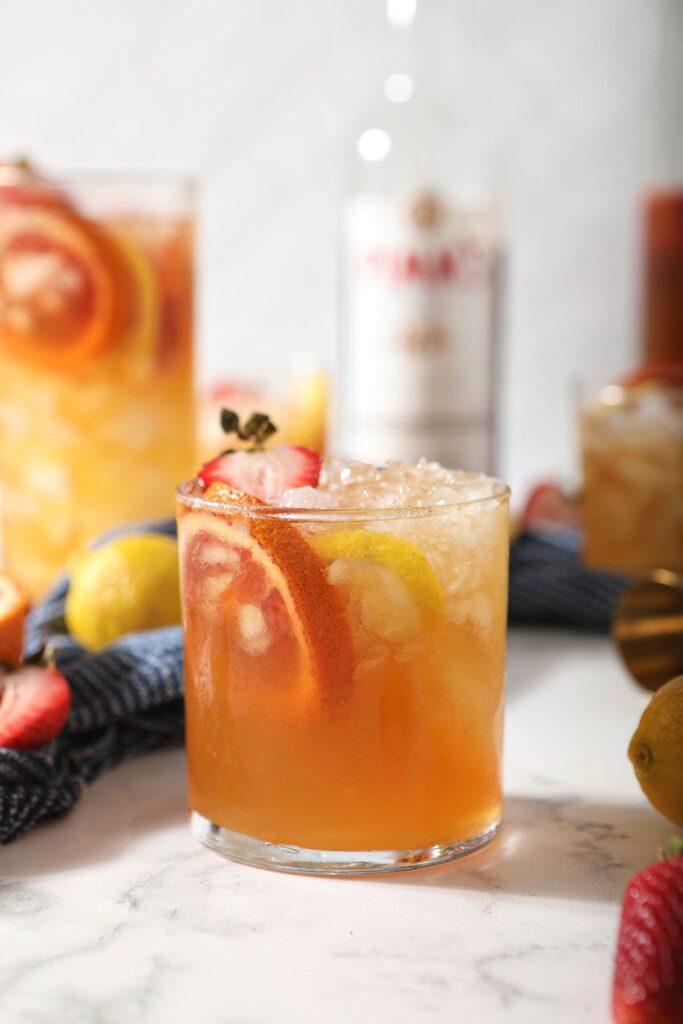 A glass of a Pimms drink garnished with blood orange, lemon and strawberry