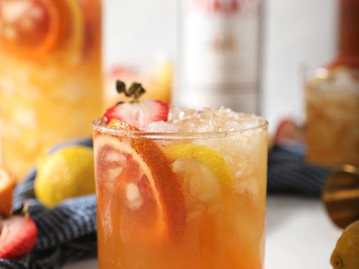 A glass of a Pimms drink garnished with blood orange, lemon and strawberry