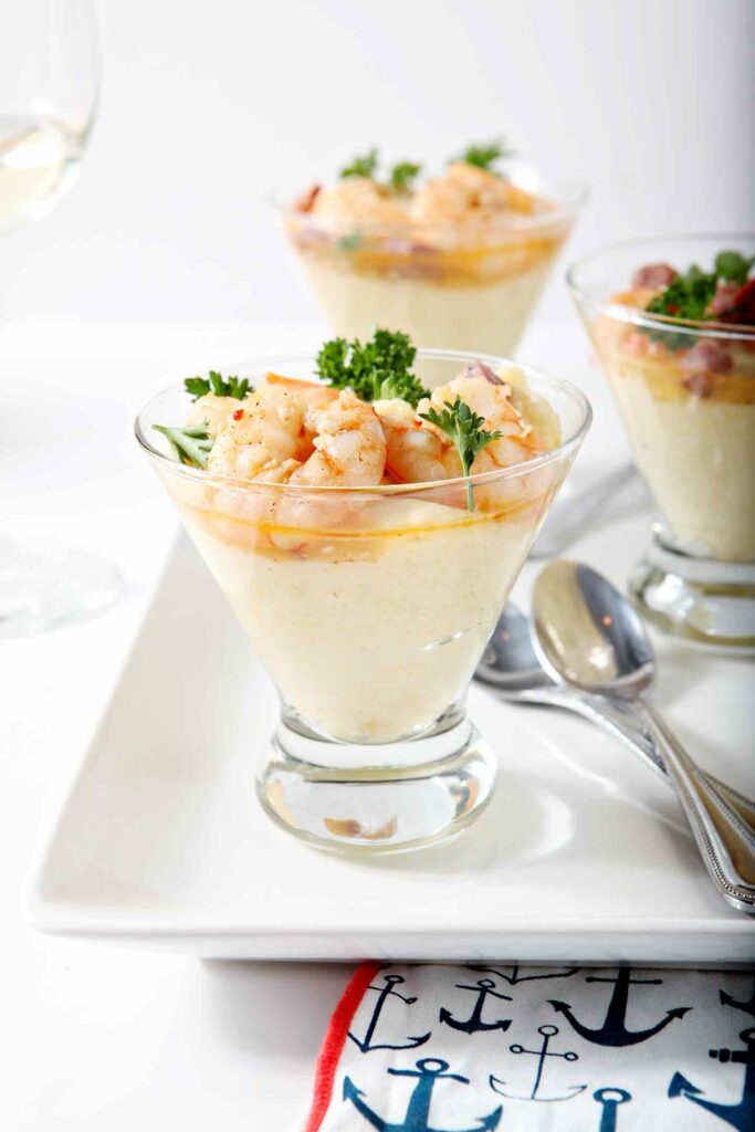 Three cups holding Cajun shrimp and grits on a white platter with spoons