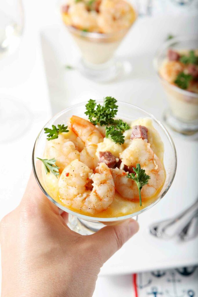 A woman holds a glass of shrimp and grits garnished with parsley