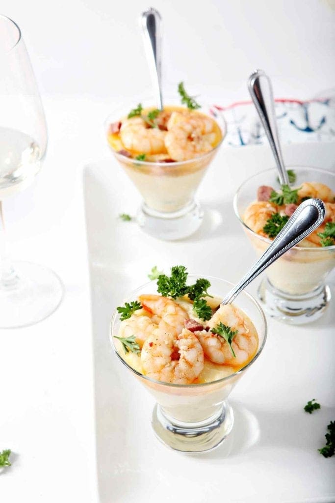 Three cups holding shrimp and grits are on a white platter ready for serving