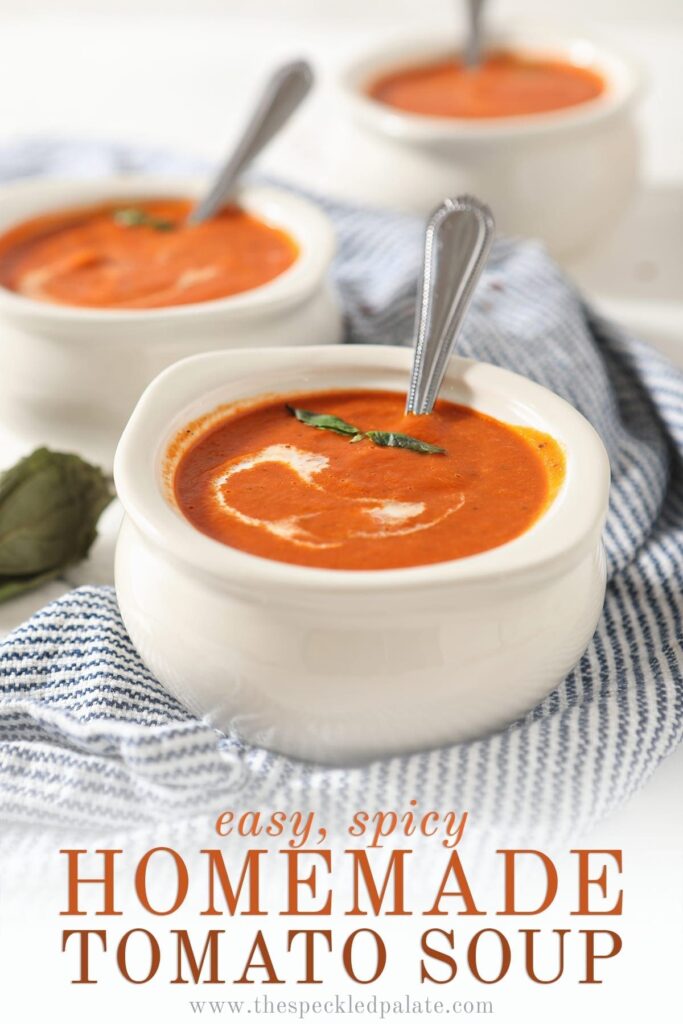 Close up of a white bowl holding spicy tomato soup with a swirl of cream and basil leaves on top with the text 'easy, spicy homemade tomato soup'