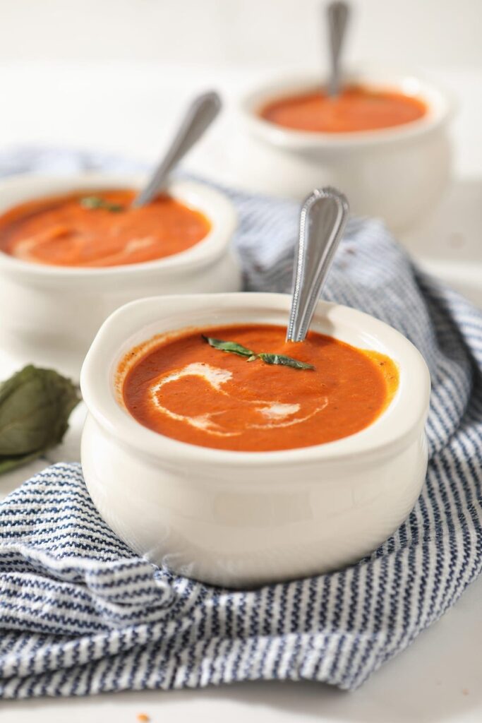 Close up of a white bowl holding spicy tomato soup with a swirl of cream and basil leaves on top