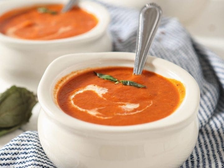 Close up of a white bowl holding spicy tomato soup with a swirl of cream and basil leaves on top